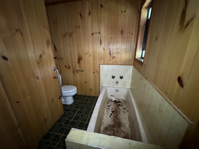 bathroom with toilet, wood walls, and a tub