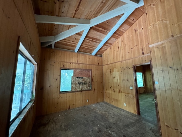 empty room with vaulted ceiling with beams, wood walls, and a wealth of natural light