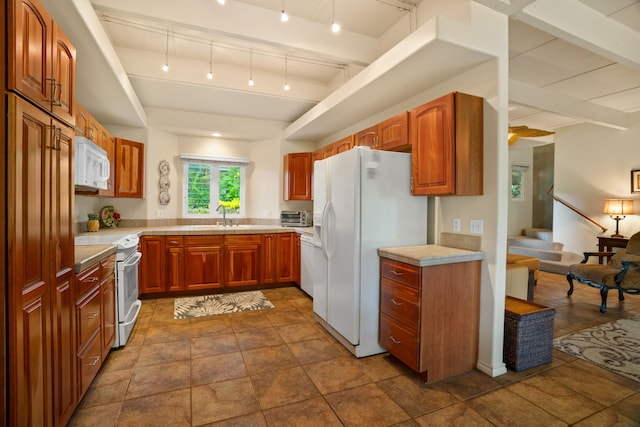 kitchen featuring dark tile patterned floors, track lighting, beam ceiling, sink, and white appliances