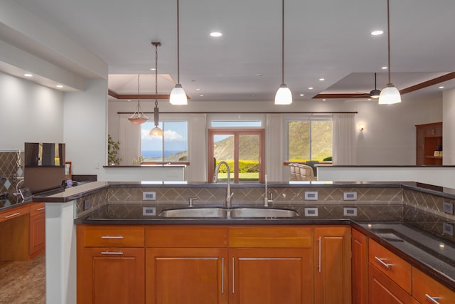 kitchen featuring decorative backsplash, hanging light fixtures, dark stone counters, and sink