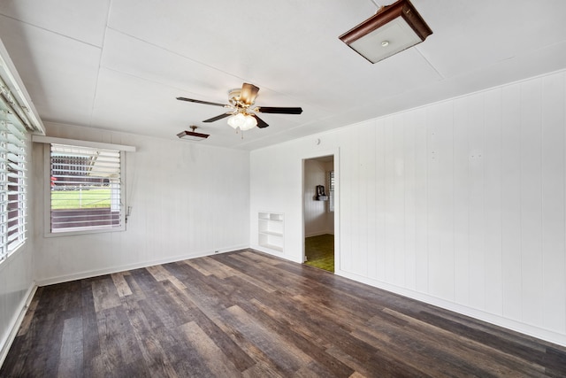 empty room with ceiling fan, wood walls, and dark hardwood / wood-style flooring