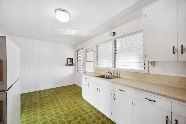 kitchen featuring white cabinets, white fridge, wooden walls, and sink