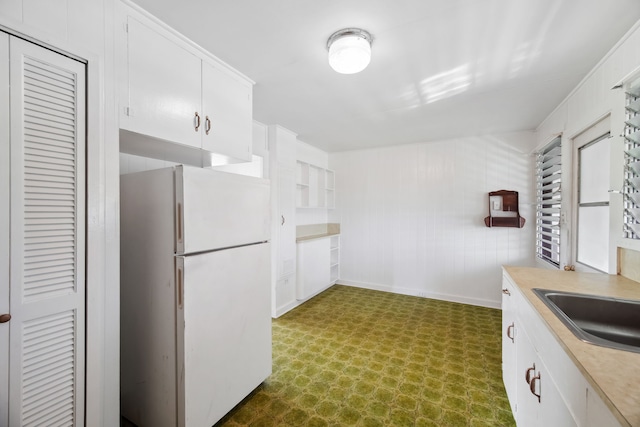 kitchen with white cabinets, white refrigerator, wood walls, and sink