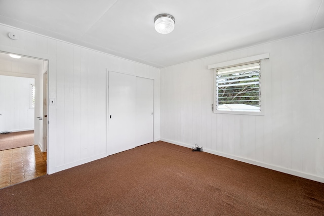 unfurnished bedroom with carpet, a closet, and wood walls