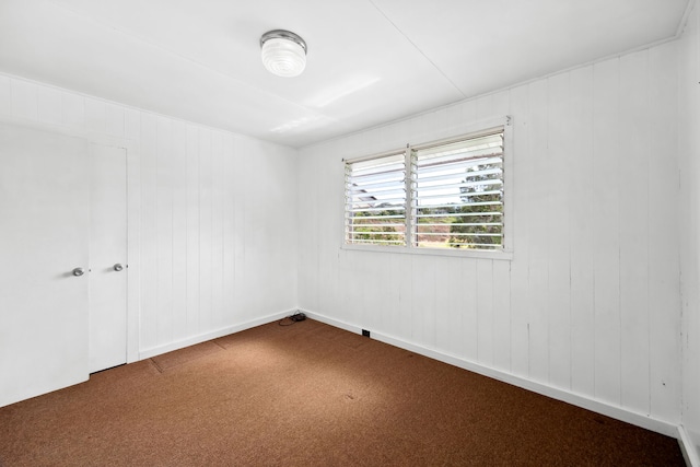 unfurnished room featuring carpet and wooden walls