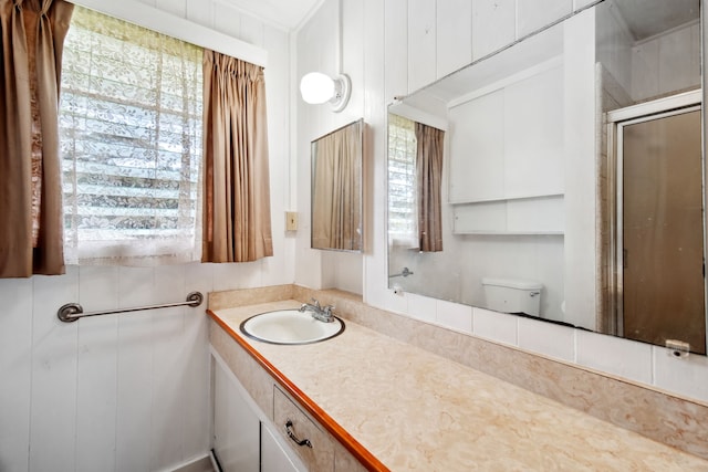 bathroom with vanity, toilet, a shower with door, and wood walls