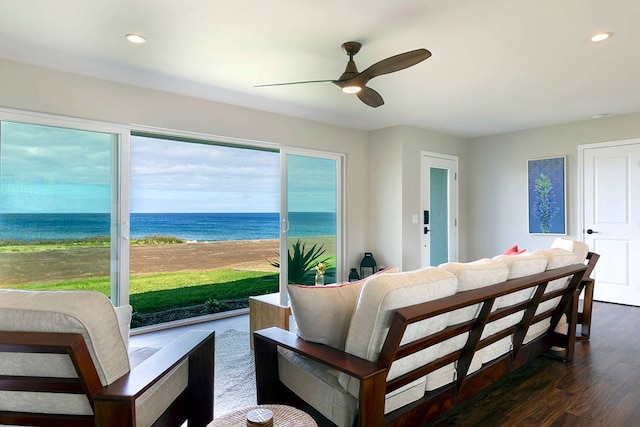 living room with ceiling fan, a water view, dark wood-type flooring, and a beach view