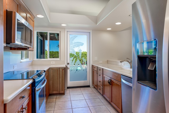 kitchen with light tile patterned flooring, stainless steel appliances, a tray ceiling, and sink