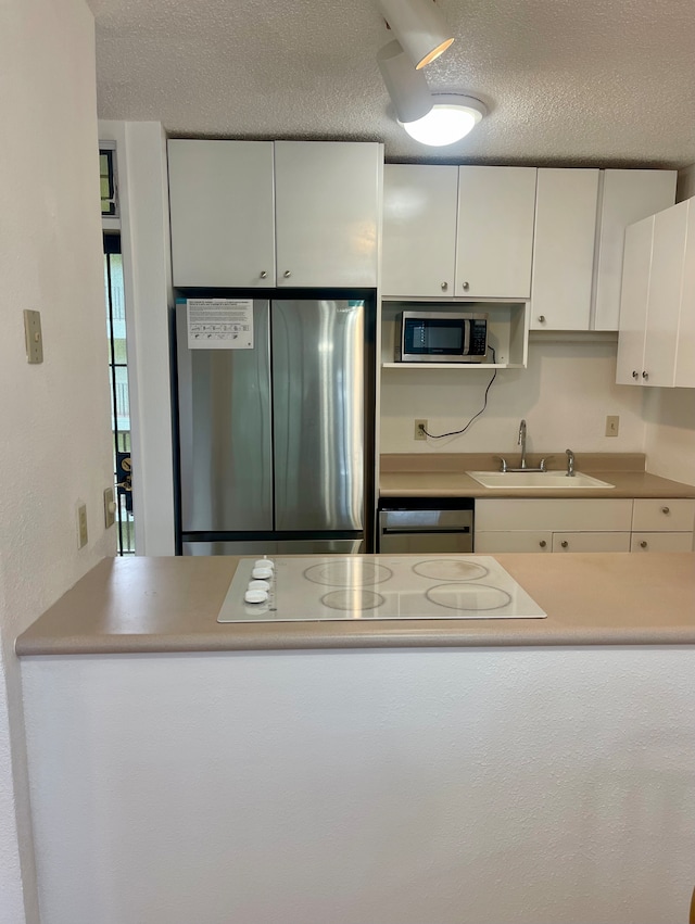 kitchen featuring stainless steel appliances, white cabinets, sink, and a textured ceiling