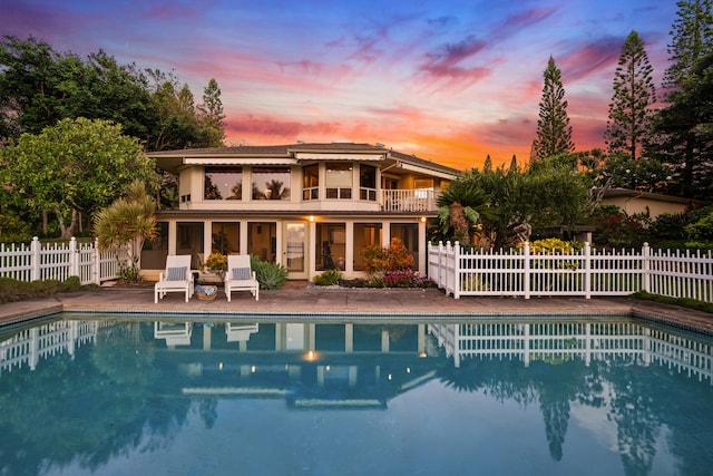 back house at dusk with a patio, a balcony, and a fenced in pool