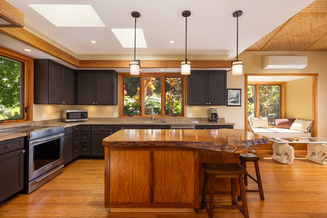 kitchen with light wood-type flooring, appliances with stainless steel finishes, a wall mounted AC, and a center island