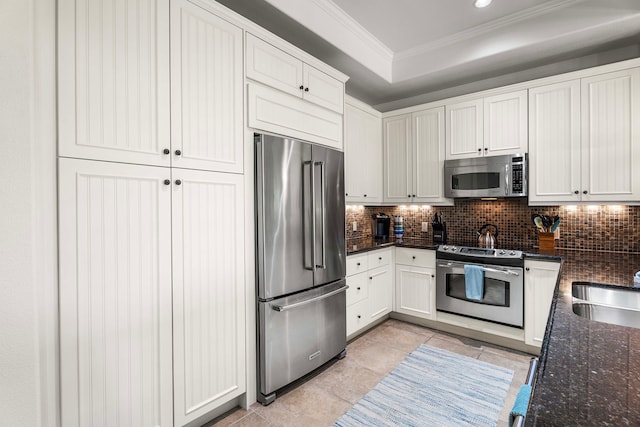 kitchen featuring decorative backsplash, appliances with stainless steel finishes, dark stone counters, ornamental molding, and white cabinets