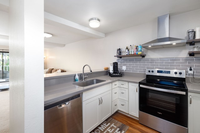 kitchen with sink, tasteful backsplash, wall chimney range hood, white cabinetry, and appliances with stainless steel finishes