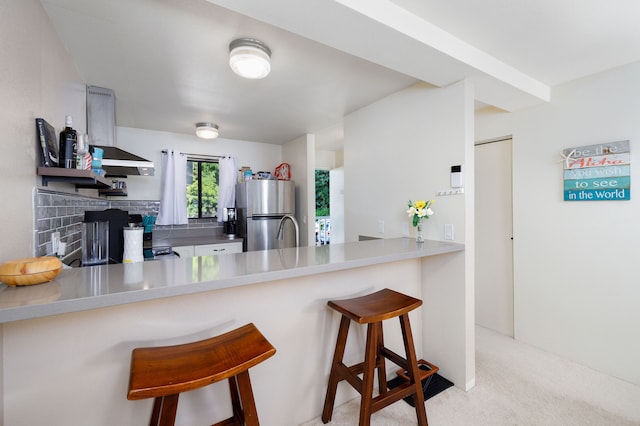 kitchen with light carpet, a breakfast bar, kitchen peninsula, range hood, and stainless steel fridge