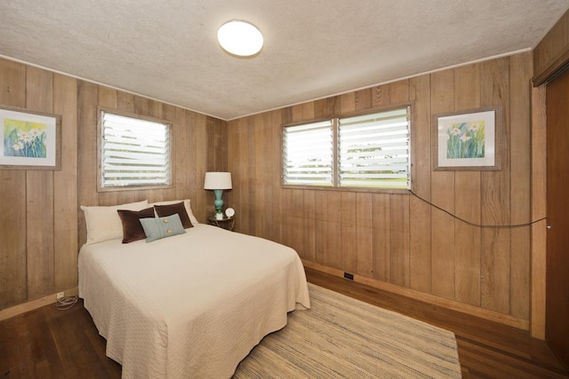 bedroom featuring hardwood / wood-style flooring, wooden walls, and a textured ceiling