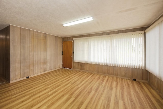 unfurnished room featuring wooden walls, a textured ceiling, and light hardwood / wood-style flooring