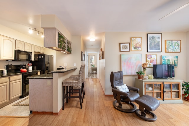 kitchen featuring dark stone counters, black appliances, light wood-type flooring, a kitchen bar, and kitchen peninsula