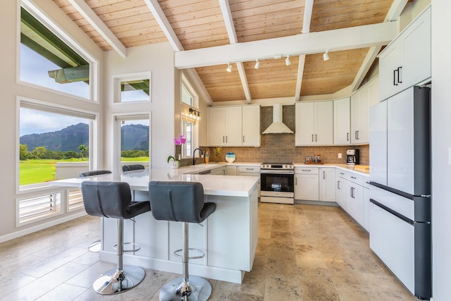 kitchen with wall chimney exhaust hood, stainless steel stove, beamed ceiling, white fridge, and white cabinetry