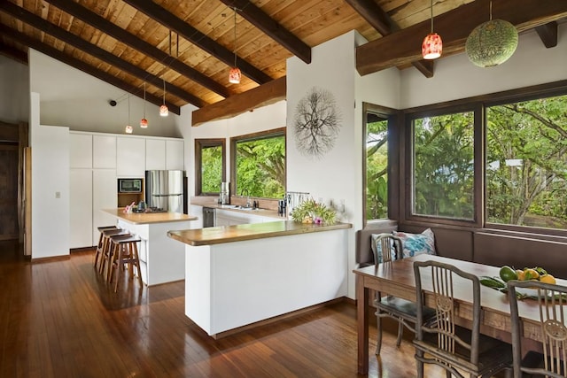 kitchen featuring wood ceiling, built in microwave, beam ceiling, white cabinetry, and stainless steel refrigerator