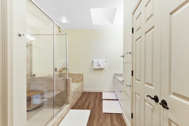 bathroom featuring hardwood / wood-style floors, vanity, plus walk in shower, and a skylight