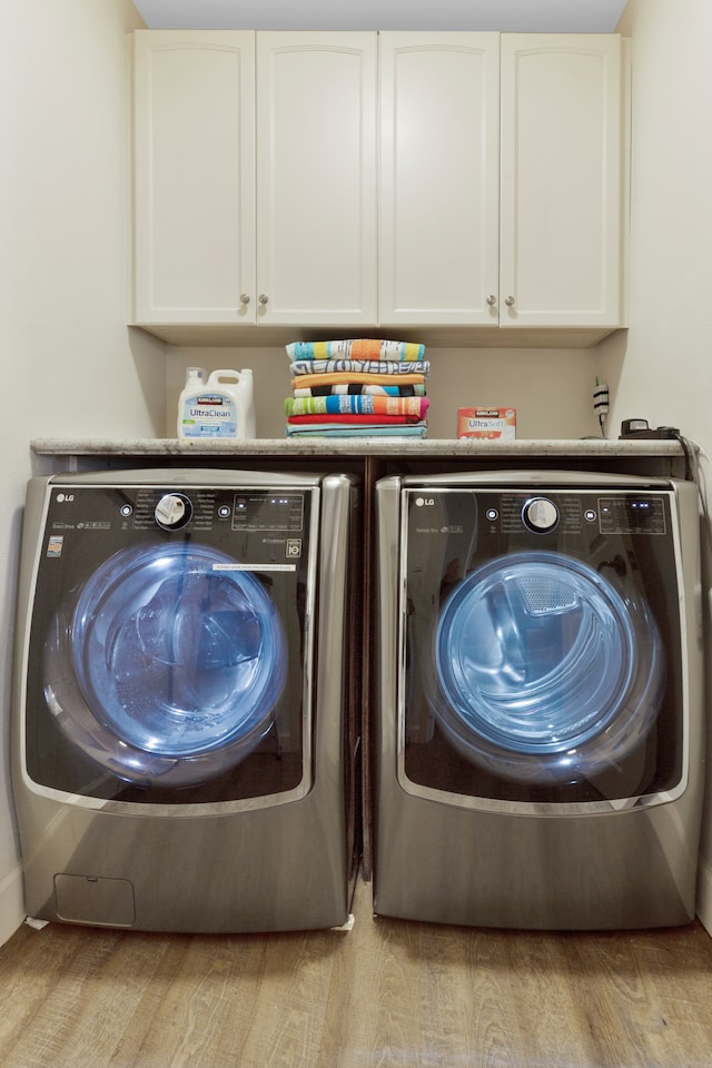 washroom with separate washer and dryer, cabinets, and light wood-type flooring