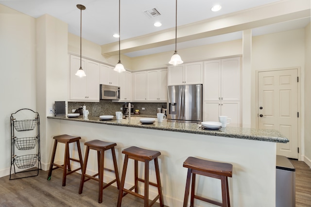 kitchen featuring white cabinets, kitchen peninsula, dark hardwood / wood-style floors, appliances with stainless steel finishes, and dark stone countertops