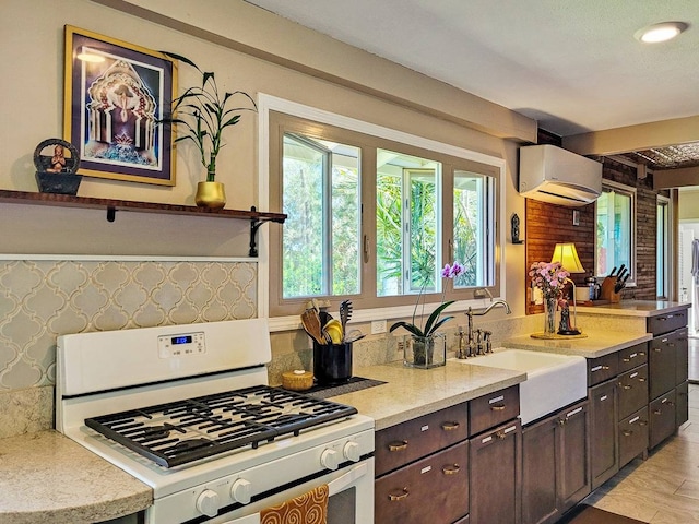 kitchen with white range with gas stovetop, dark brown cabinets, sink, and a wall mounted air conditioner