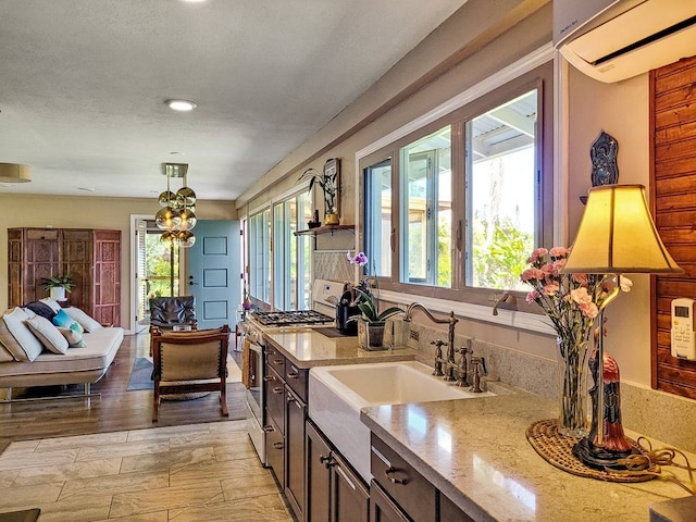 kitchen featuring a wall unit AC, light hardwood / wood-style floors, gas stove, light stone countertops, and decorative light fixtures