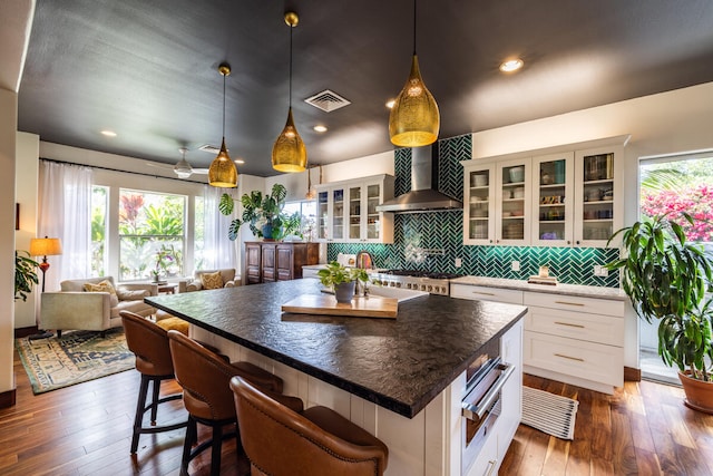 kitchen featuring wall chimney exhaust hood, a breakfast bar, a center island, dark hardwood / wood-style floors, and white cabinetry