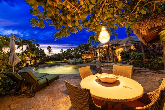 patio terrace at dusk featuring a swimming pool with hot tub