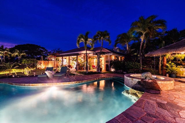 pool at night featuring an in ground hot tub and a patio