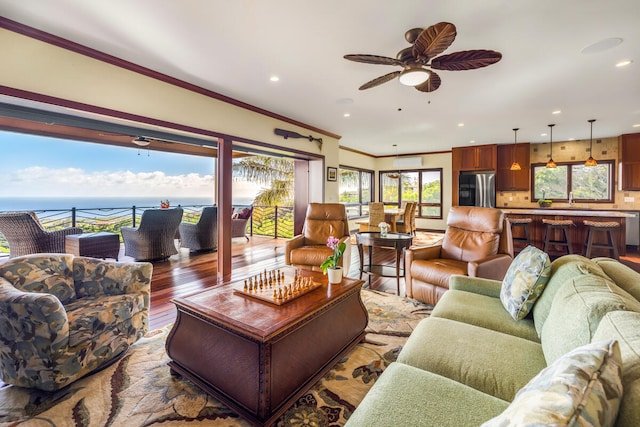 living room featuring ceiling fan, hardwood / wood-style floors, a water view, and ornamental molding