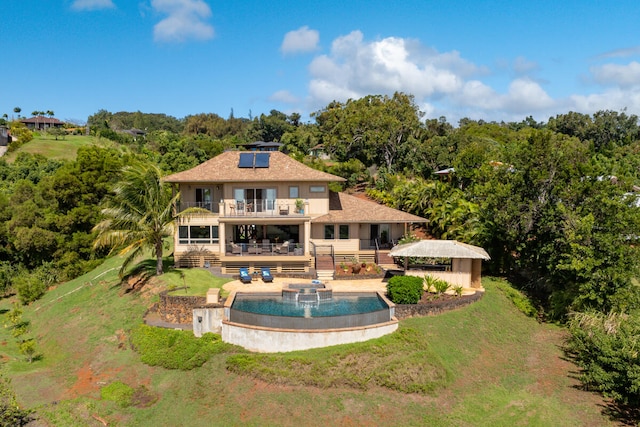 back of property featuring a lawn, a balcony, a pool side deck, and solar panels