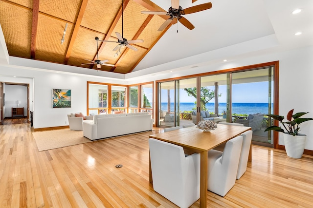 dining room with ceiling fan, a water view, light hardwood / wood-style floors, and high vaulted ceiling