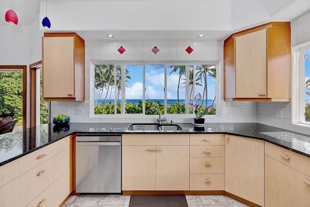 kitchen with dark stone countertops, stainless steel dishwasher, a healthy amount of sunlight, and sink