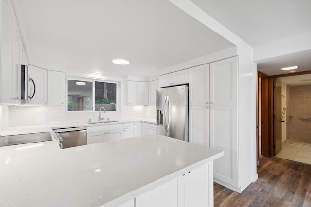 kitchen with kitchen peninsula, dark hardwood / wood-style flooring, stainless steel appliances, sink, and white cabinetry