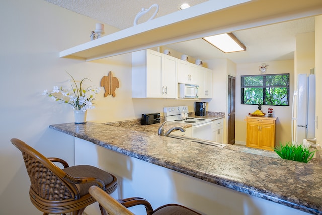 kitchen featuring white appliances, white cabinets, a textured ceiling, kitchen peninsula, and a breakfast bar area