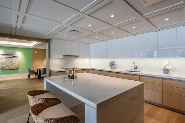 kitchen with light hardwood / wood-style floors, white cabinetry, a kitchen island, and sink