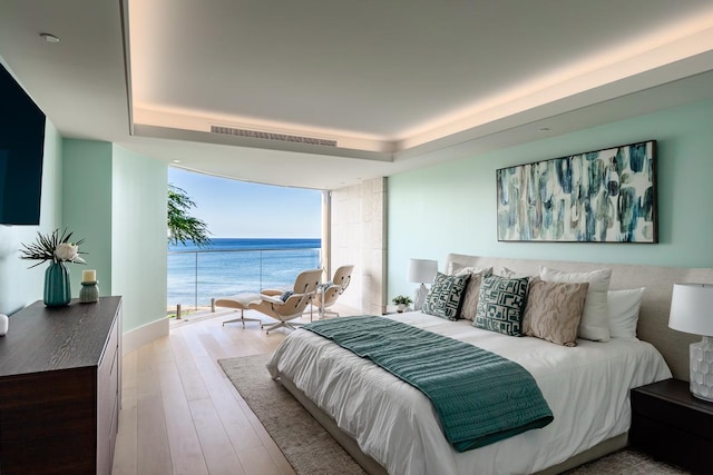 bedroom with a raised ceiling, light hardwood / wood-style flooring, and a water view