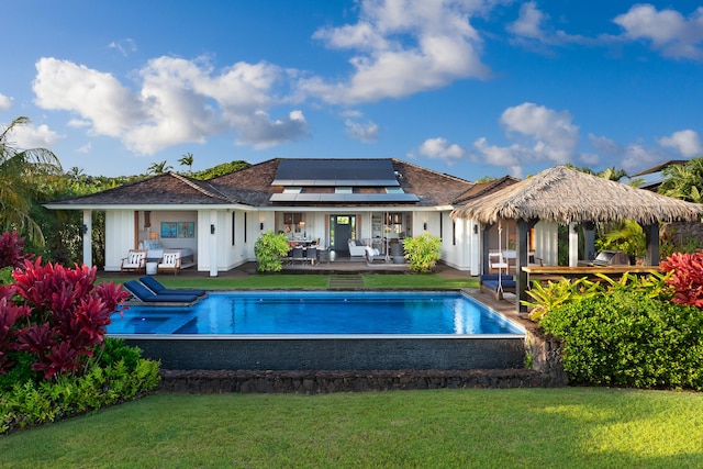 rear view of property featuring a lawn, solar panels, a patio area, and a swimming pool side deck