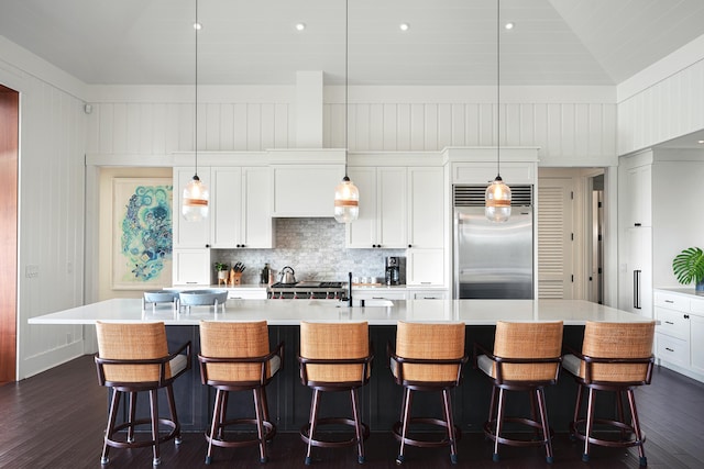 kitchen featuring dark wood-type flooring, stainless steel appliances, a large island with sink, pendant lighting, and a breakfast bar area