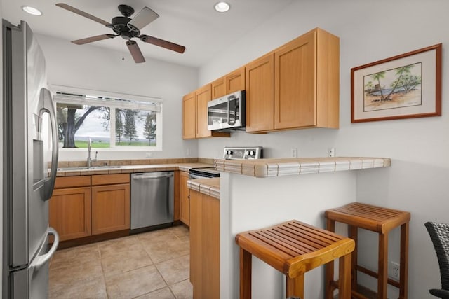 kitchen featuring ceiling fan, stainless steel appliances, a kitchen breakfast bar, tile countertops, and kitchen peninsula