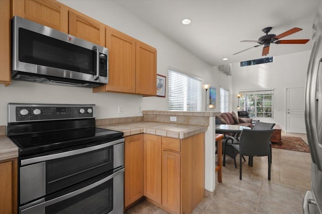 kitchen with kitchen peninsula, appliances with stainless steel finishes, ceiling fan, tile countertops, and light tile patterned flooring