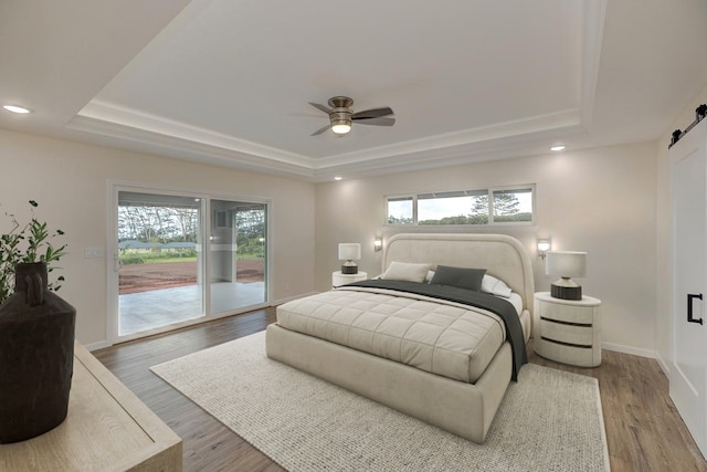 bedroom featuring a raised ceiling, a barn door, wood-type flooring, and access to exterior