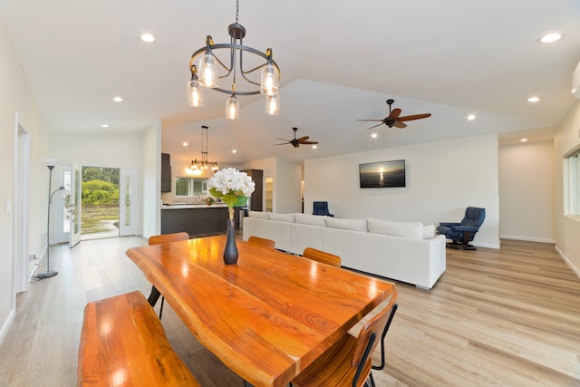 dining space with ceiling fan with notable chandelier, light hardwood / wood-style floors, and vaulted ceiling