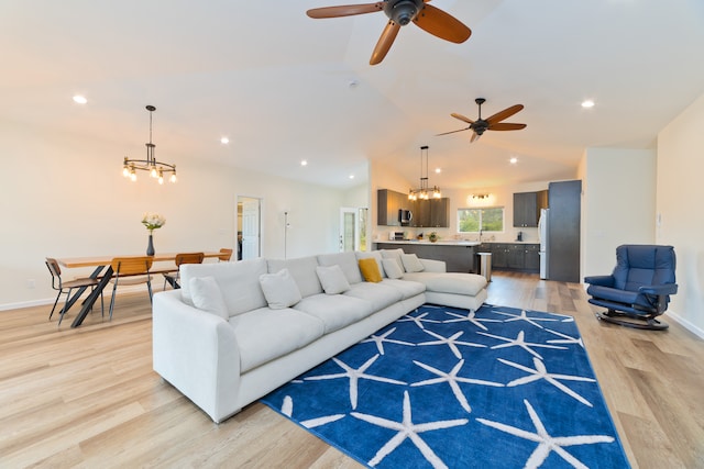 living room with ceiling fan with notable chandelier, light hardwood / wood-style floors, and lofted ceiling