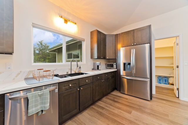 kitchen featuring dark brown cabinetry, sink, lofted ceiling, appliances with stainless steel finishes, and light wood-type flooring