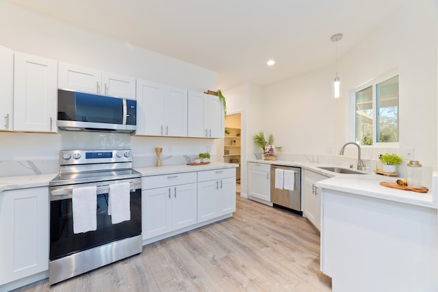 kitchen with white cabinetry, sink, hanging light fixtures, stainless steel appliances, and light hardwood / wood-style flooring