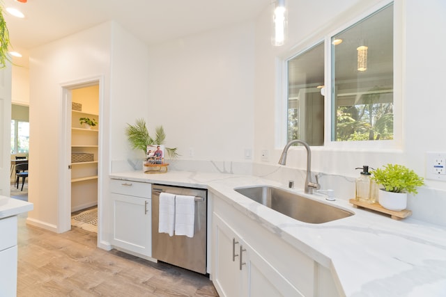 kitchen with light stone counters, stainless steel dishwasher, sink, light hardwood / wood-style flooring, and hanging light fixtures