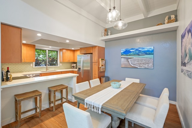 dining space with light wood-type flooring, sink, and beamed ceiling